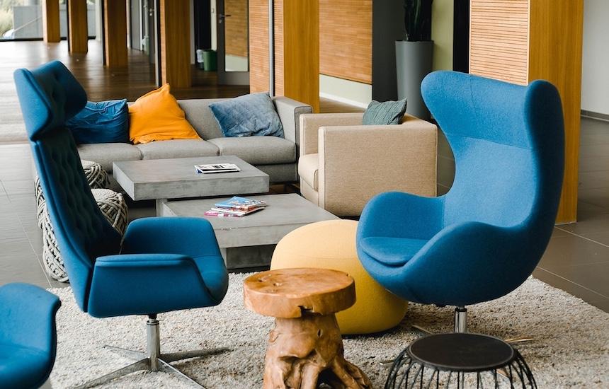 Zwei leere Sessel stehen um einen kleinen Holztisch herum, dahinter sind Sofas mit Kissen zu sehen