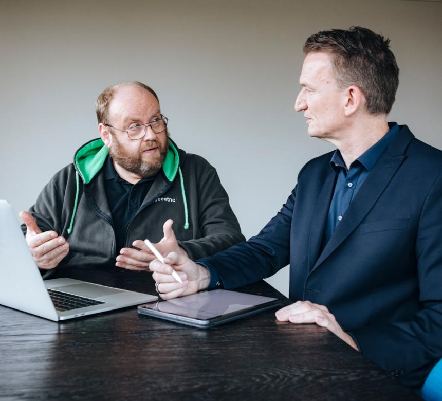 2 Männer am Tisch im Beratungsgespräch, vor ihnen Notebook und Tablet