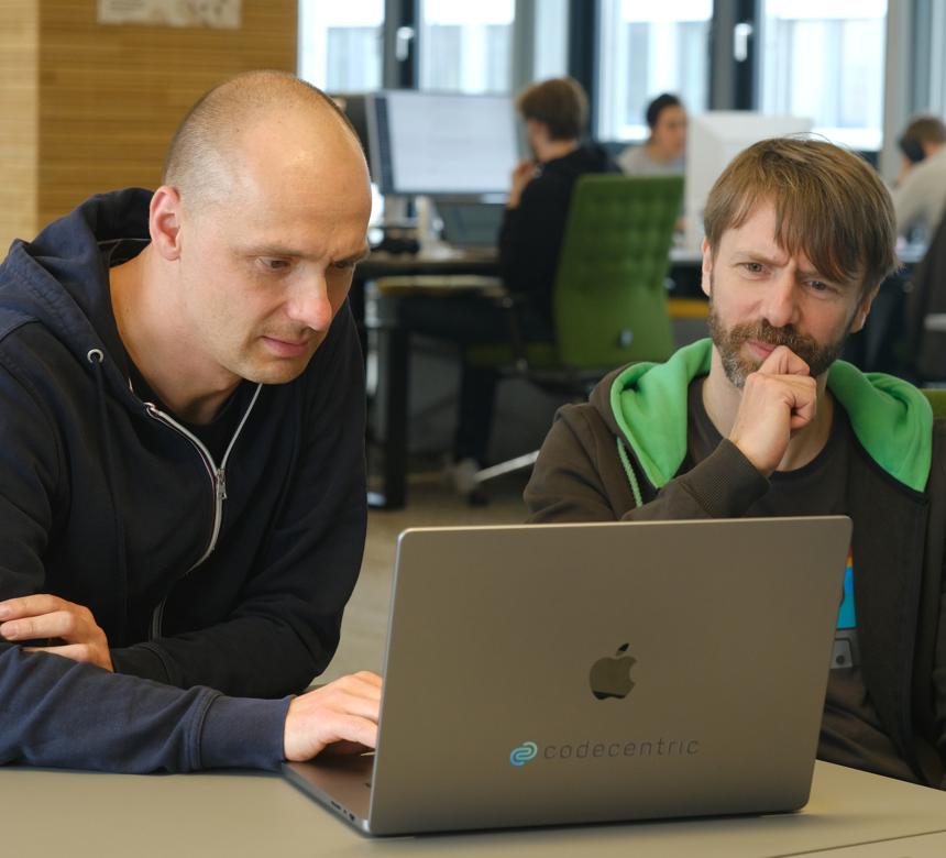 Zwei Personen sitzen an einem Laptop zusammen und denken intensiv nach