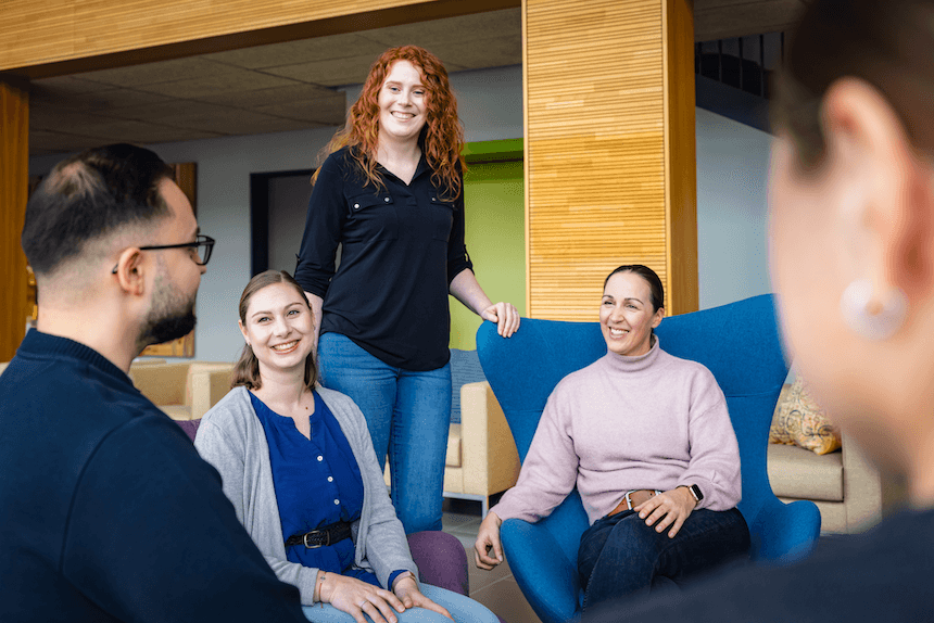 A group of diverse colleagues smiling and chatting together in a modern, comfortable office lounge.