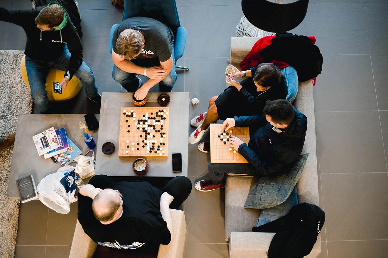 Eine Gruppe Menschen von oben fotografiert, die auf Sofas sitzen, sich unterhalten und Brettspiele spielen