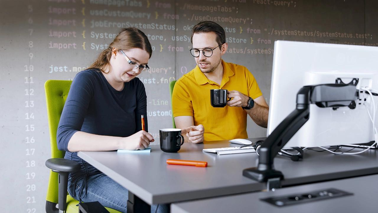 2 codecentricer die am Schreibtisch zusammen arbeiten, im Hintergrund Programmier-Codes