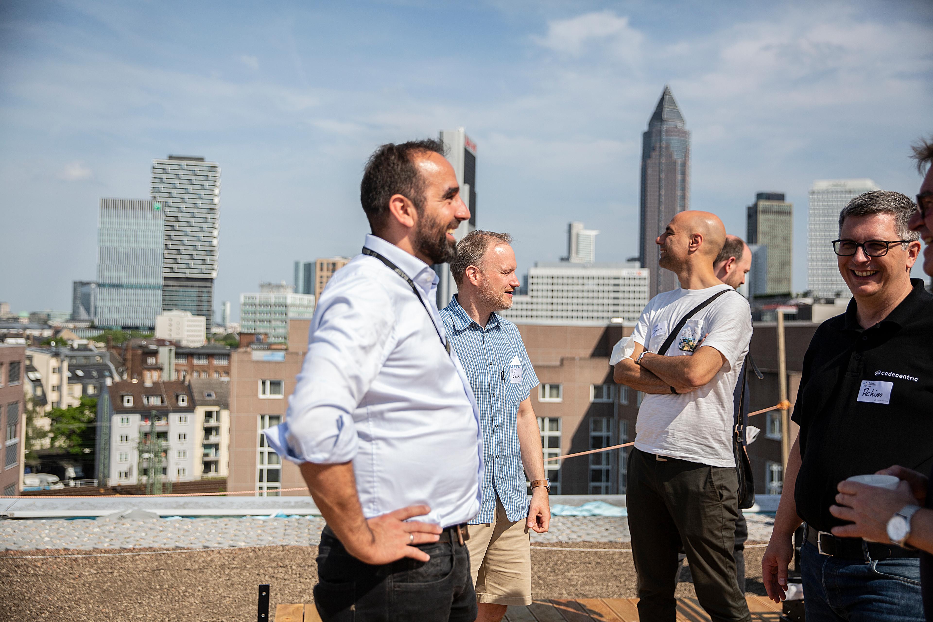 Mehrere Personen, die auf einer Dachterrasse stehen und sich unterhalten, darunter codecentricer.