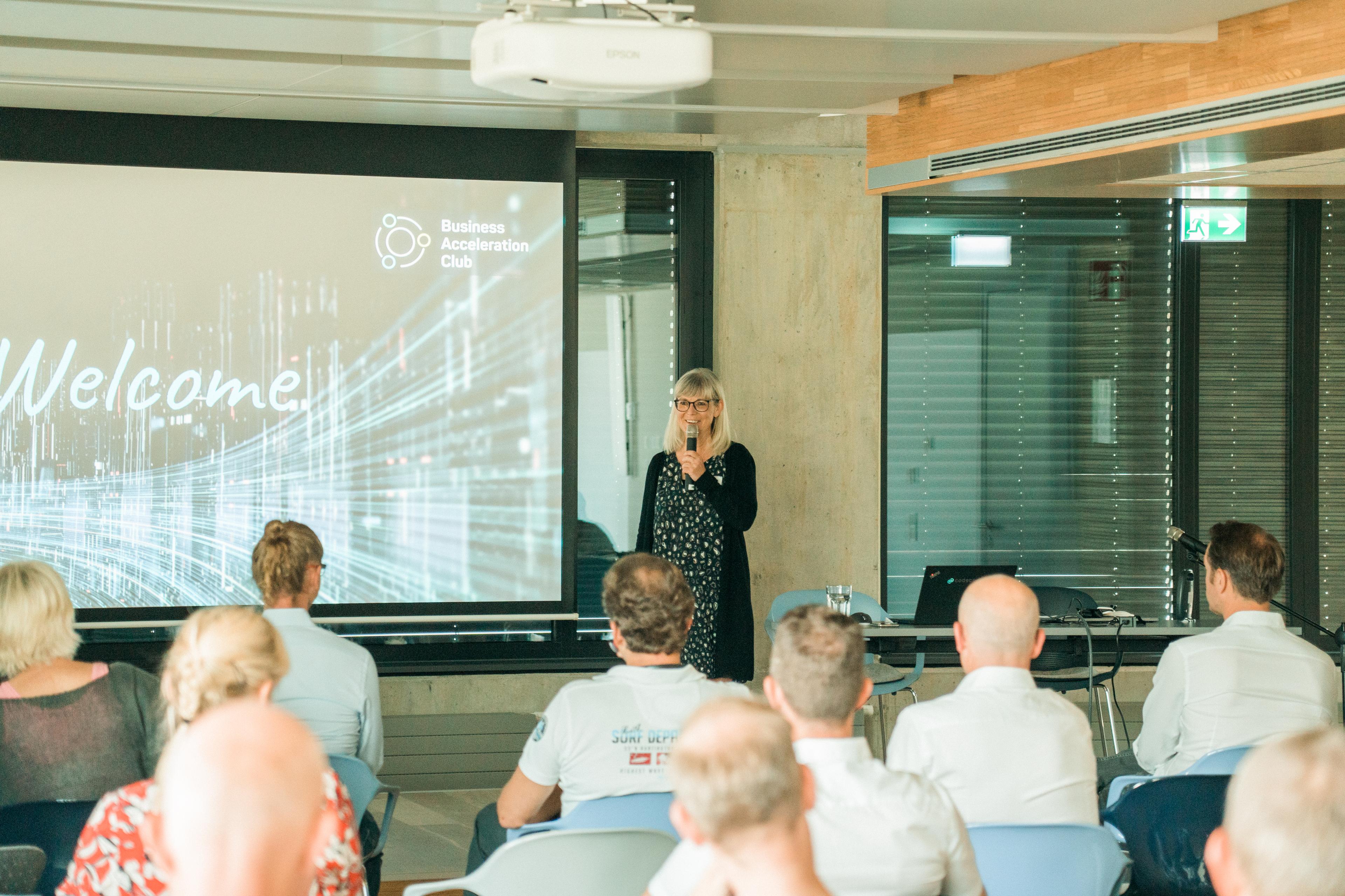 Eine Frau, die einen Vortrag zum Business Acceleration Club hält und einem Publikum, welches diesem gespannt zuhört.