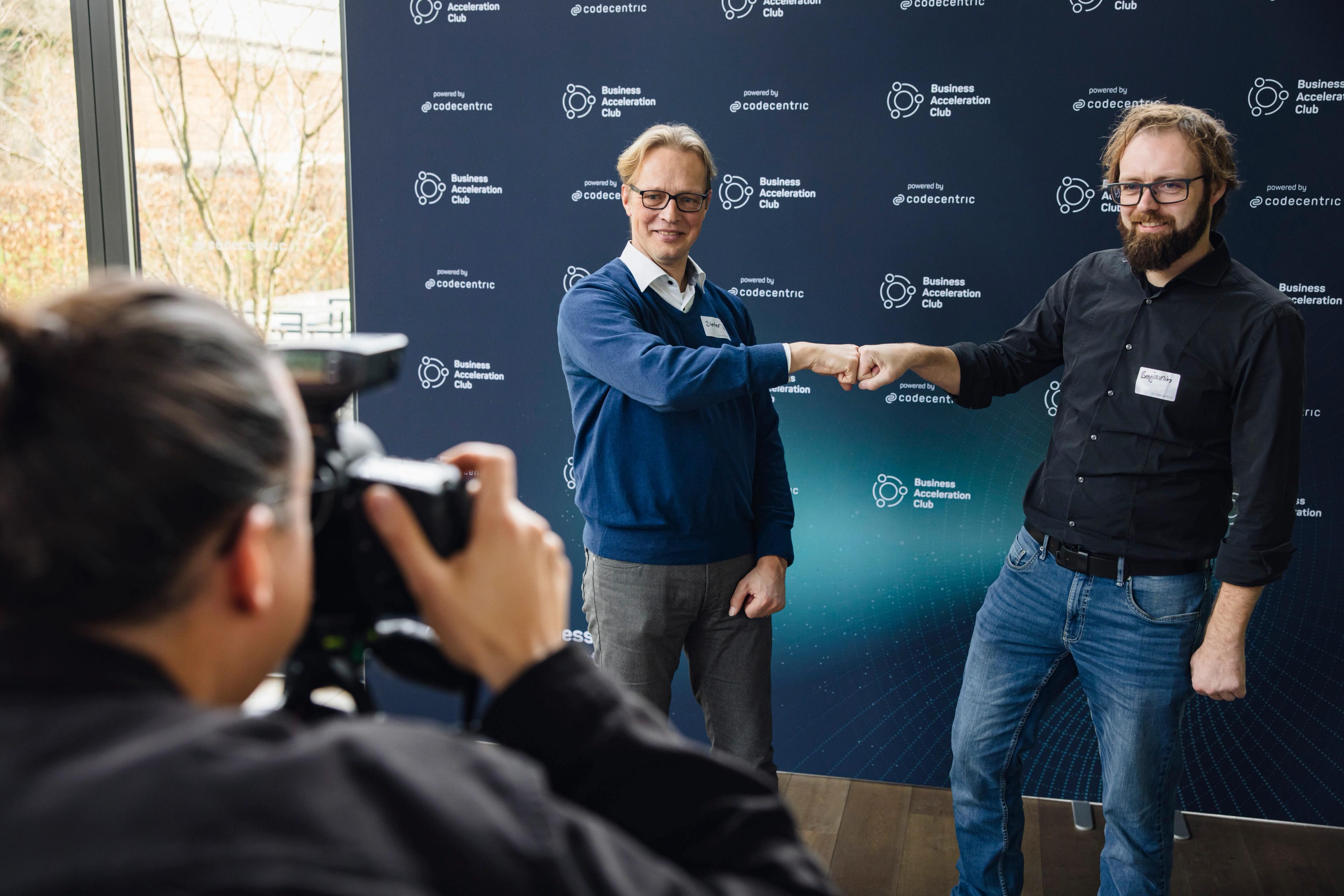 2 Personen, die vor Wand des Business Acceleration Club und der codecentric ein Foto machen, bei dem sie sich die Faust geben