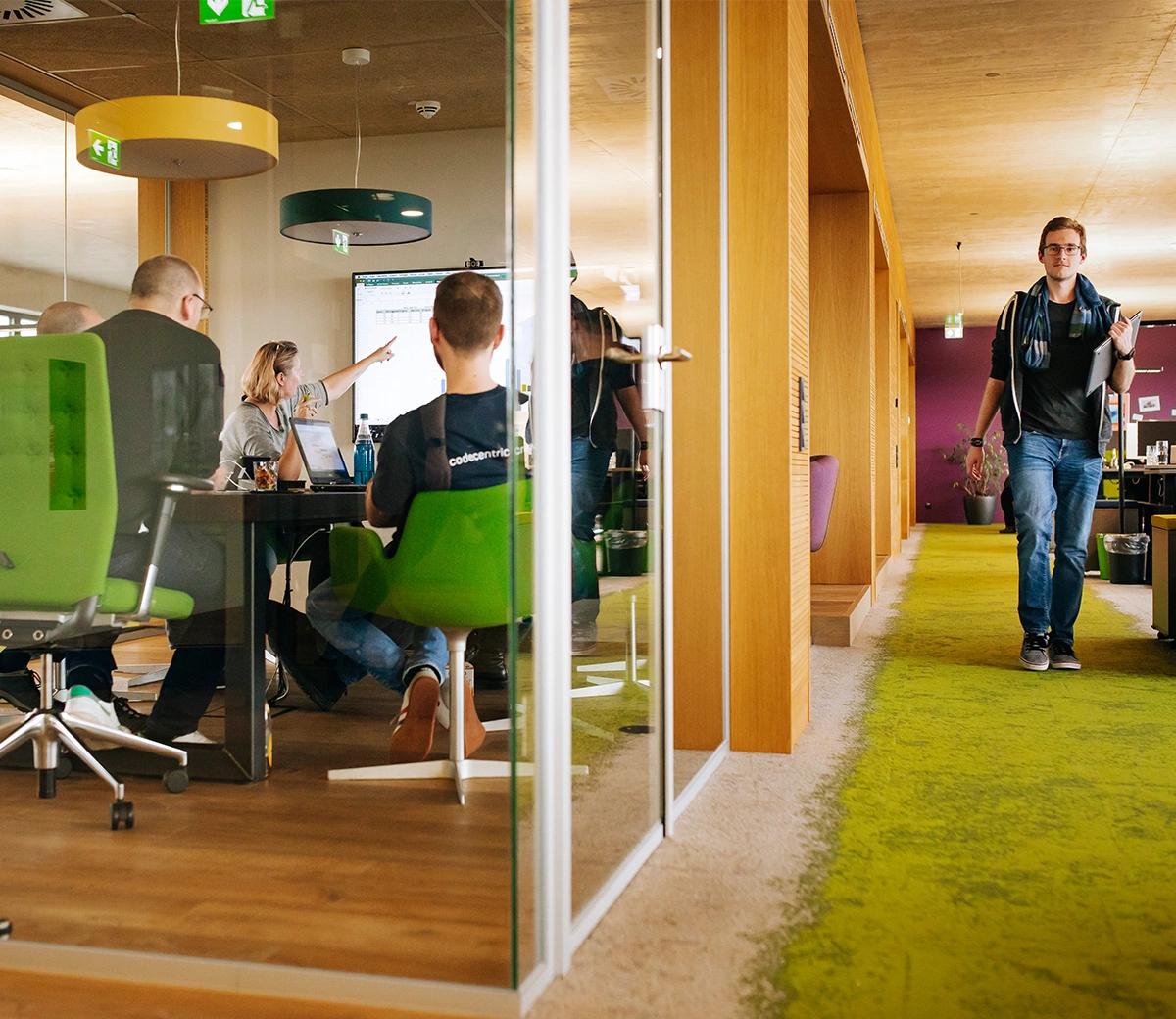 Mehrere codecentricer in einem Meeting-Raum, ein weiterer läuft außen an diesem vorbei.